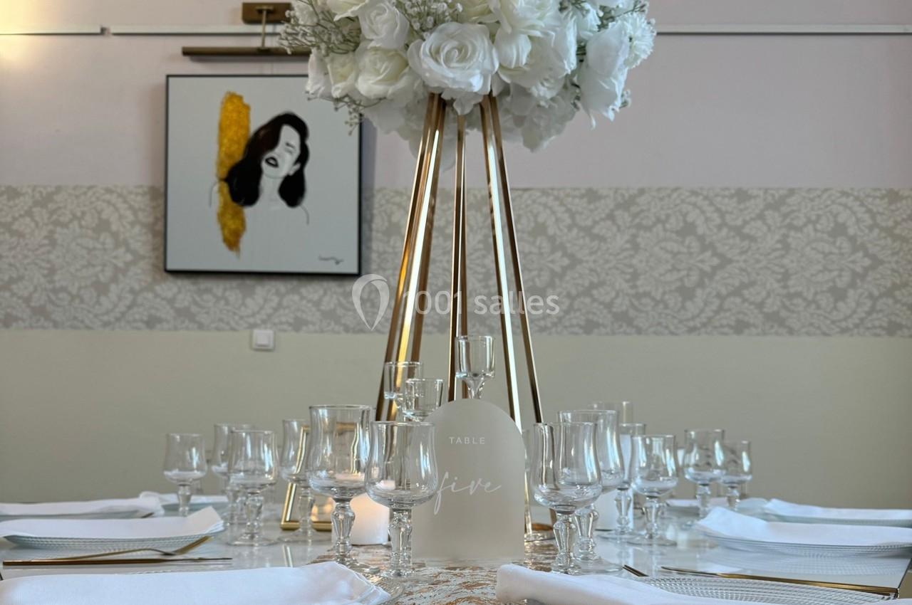 Centre de table élégant avec des fleurs blanches sur un support doré, entouré de verres et de couverts.