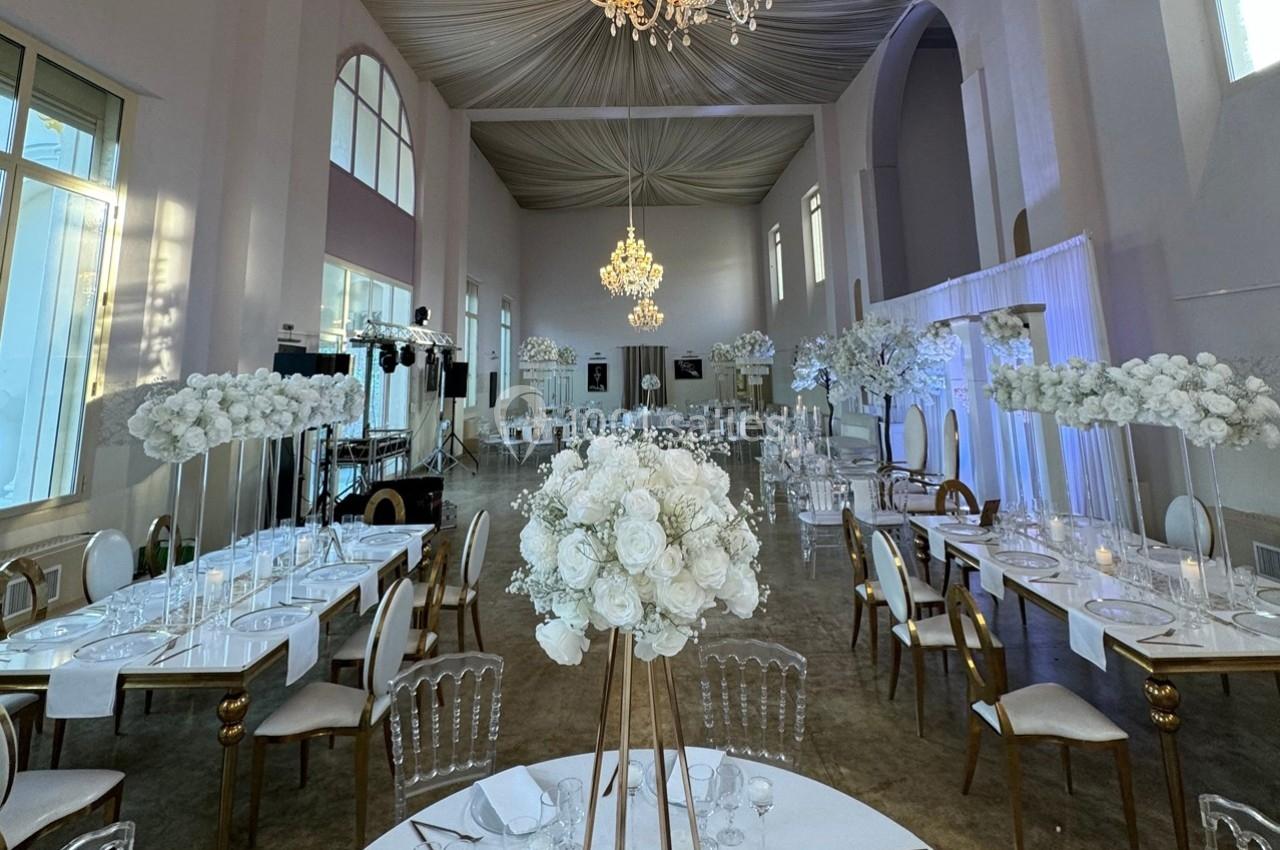 Salle de réception élégante avec tables dressées, décorations florales blanches et lustres suspendus.