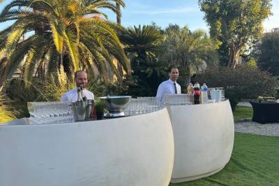 Piscine extérieure entourée de tables hautes, chaises colorées et structures gonflables, avec colline en arrière-plan.