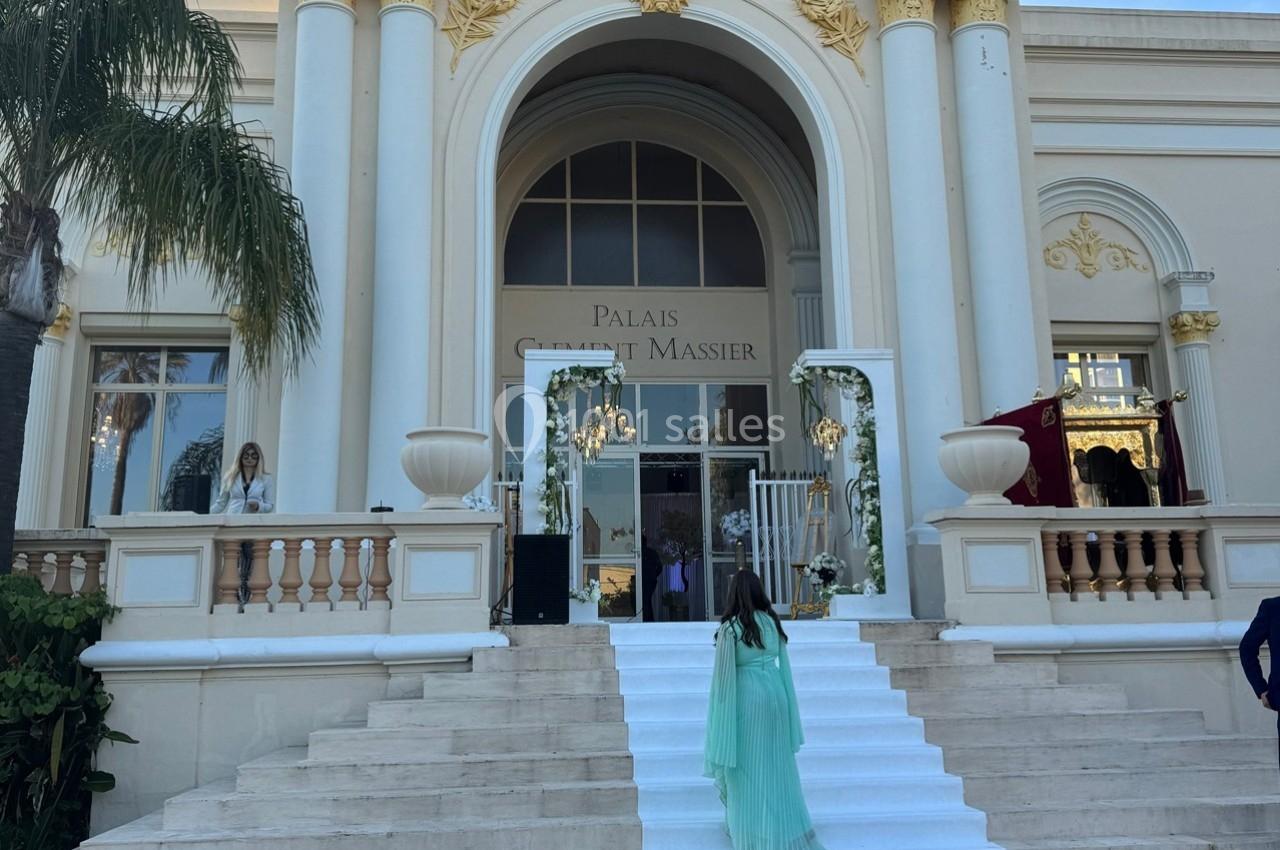 Entrée principale d'un bâtiment élégant avec colonnes et ornements dorés, escalier blanc au premier plan.