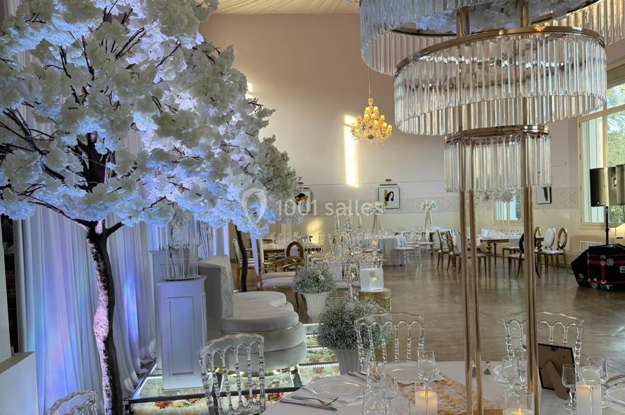 Salle de réception élégante avec tables dressées, lustres en cristal et décorations florales blanches.