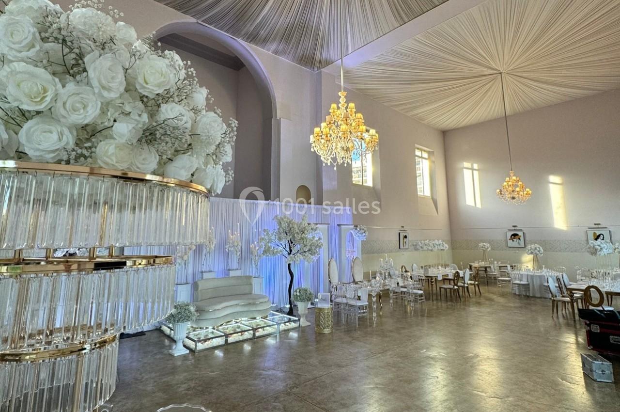 Salle de réception élégante décorée de blanc avec des lustres, des fleurs et des tables dressées.