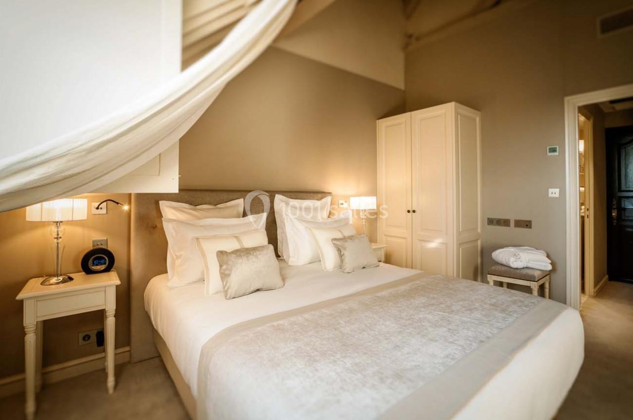 Chambre lumineuse avec lit double, draps blancs, tables de chevet, lampes et armoire dans un décor neutre et apaisant.