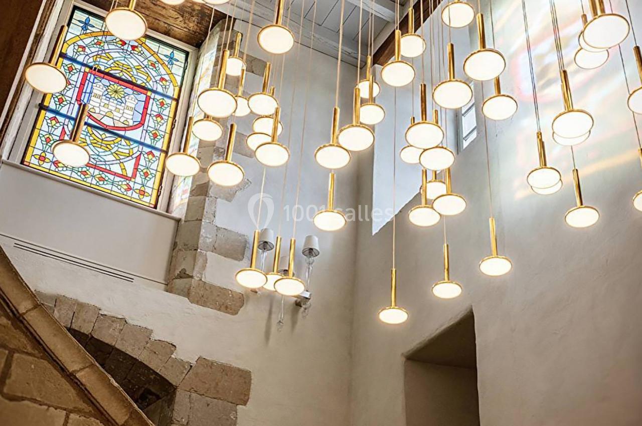 Suspension lumineuse moderne avec de multiples ampoules rondes dans un intérieur avec vitrail coloré et murs en pierre.
