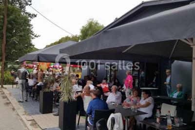 Salle sombre avec éclairage violet, plafond métallique, tables et chaises dispersées sur un sol à carreaux.