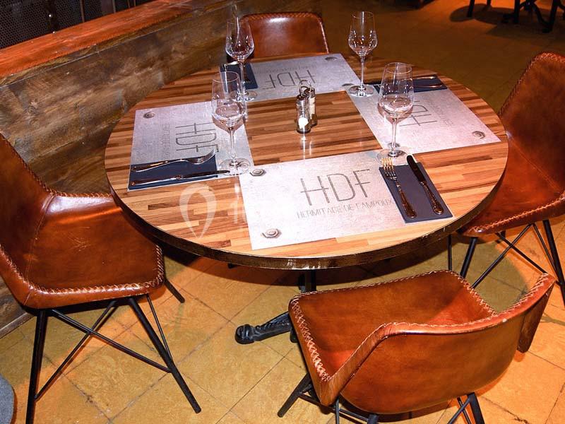 Table ronde en bois avec quatre chaises en cuir marron, dressée avec des verres, des couverts et des sets de table.