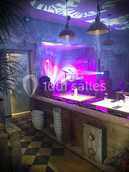 Salle de restaurant avec éclairage coloré, projecteurs violets, tables dressées et ambiance industrielle.