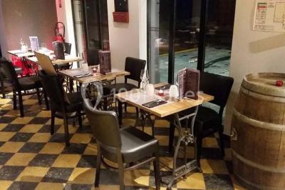 Salle sombre avec éclairage violet, plafond métallique, tables et chaises dispersées sur un sol à carreaux.