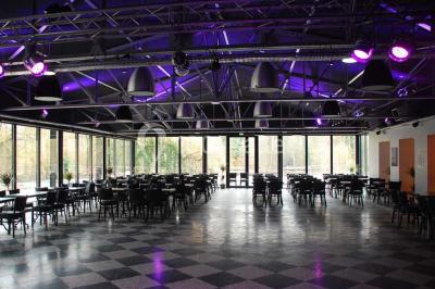 Salle sombre avec éclairage violet, plafond métallique, tables et chaises dispersées sur un sol à carreaux.