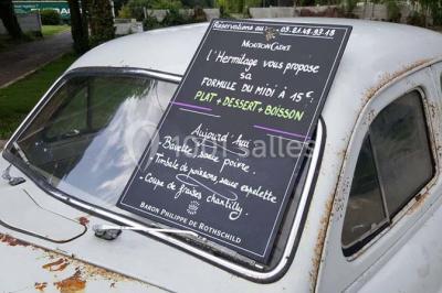 Salle sombre avec éclairage violet, plafond métallique, tables et chaises dispersées sur un sol à carreaux.