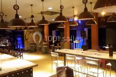 Salle sombre avec éclairage violet, plafond métallique, tables et chaises dispersées sur un sol à carreaux.