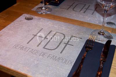 Salle sombre avec éclairage violet, plafond métallique, tables et chaises dispersées sur un sol à carreaux.