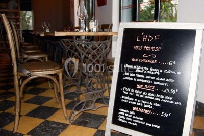 Salle sombre avec éclairage violet, plafond métallique, tables et chaises dispersées sur un sol à carreaux.