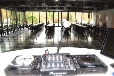 Salle sombre avec éclairage violet, plafond métallique, tables et chaises dispersées sur un sol à carreaux.