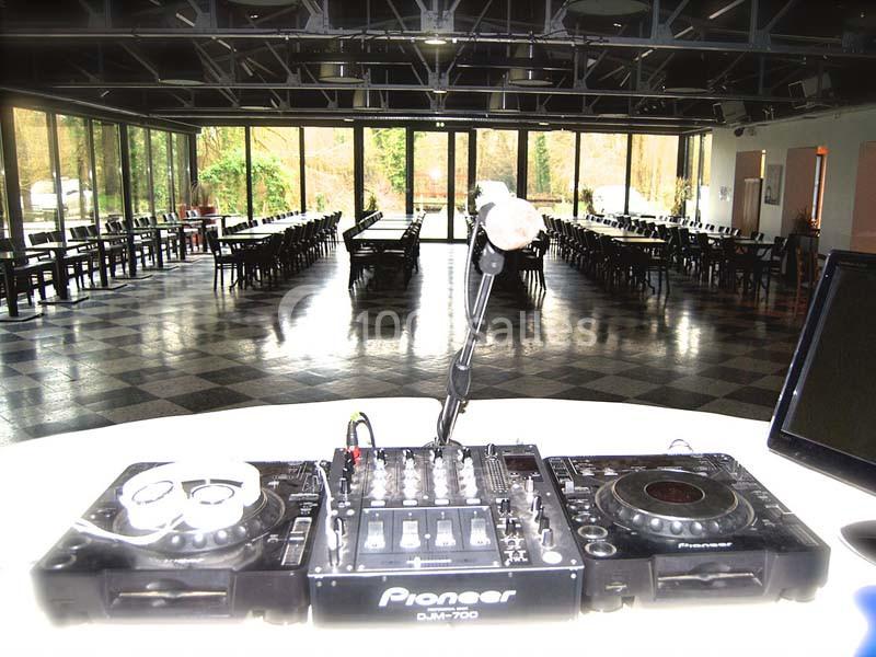 Vue depuis une table de mixage dans une grande salle avec des baies vitrées et des tables alignées.