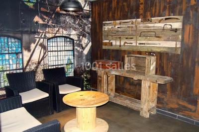 Salle sombre avec éclairage violet, plafond métallique, tables et chaises dispersées sur un sol à carreaux.