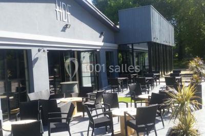 Salle sombre avec éclairage violet, plafond métallique, tables et chaises dispersées sur un sol à carreaux.