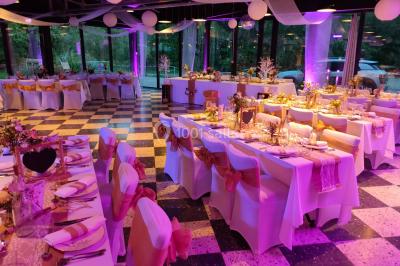 Salle sombre avec éclairage violet, plafond métallique, tables et chaises dispersées sur un sol à carreaux.
