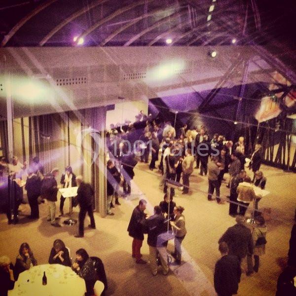 Des personnes discutent en petits groupes dans un espace intérieur moderne, éclairé par des lumières tamisées.