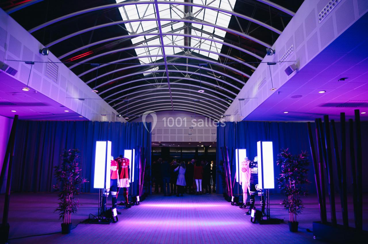 Vue d'un hall avec un plafond en verrière, éclairé par des lumières violettes, et des mannequins exposant des vêtements.