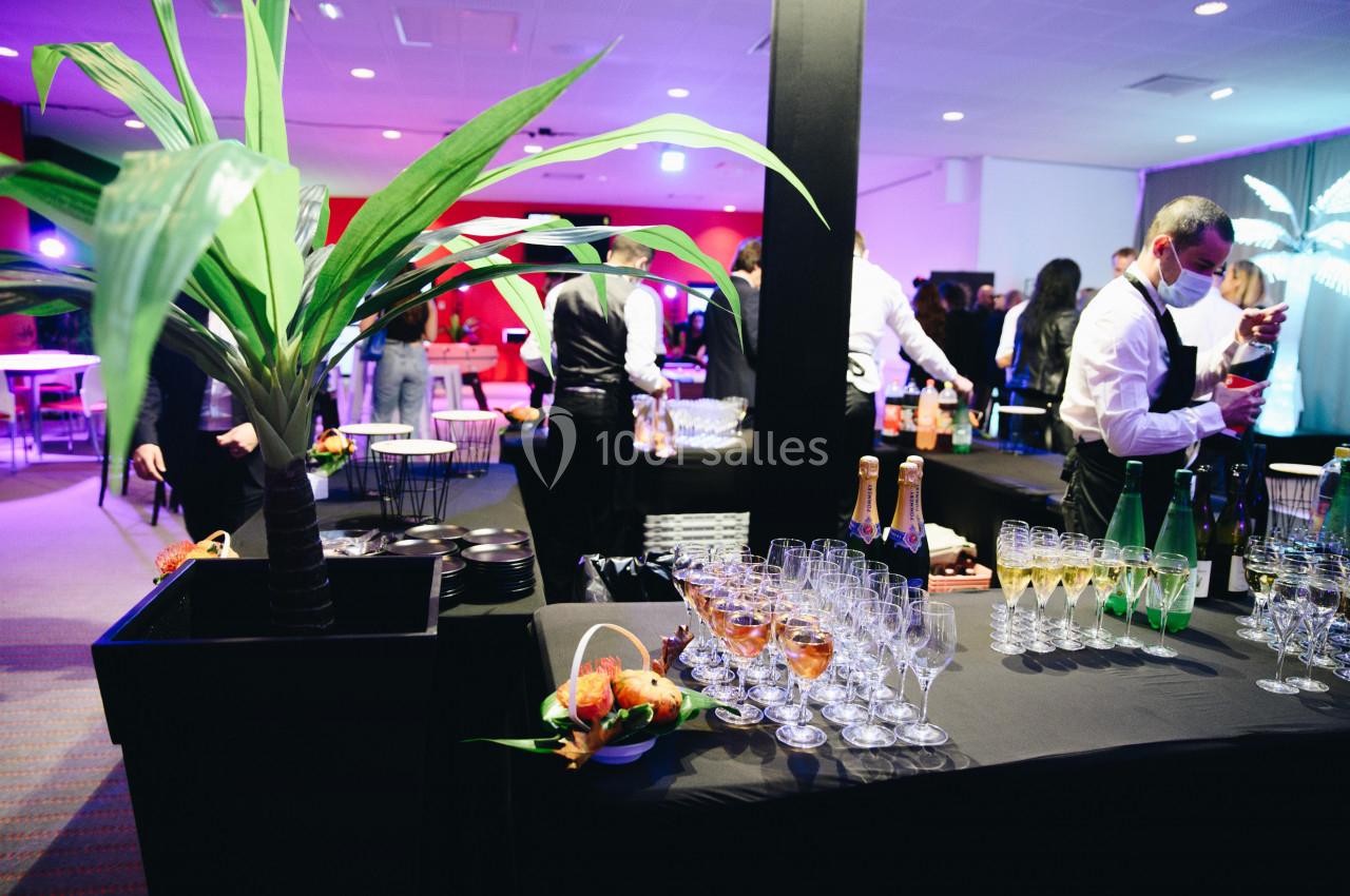 Buffet avec verres de vin, champagne et fruits exotiques, dans une salle éclairée avec des invités en arrière-plan.