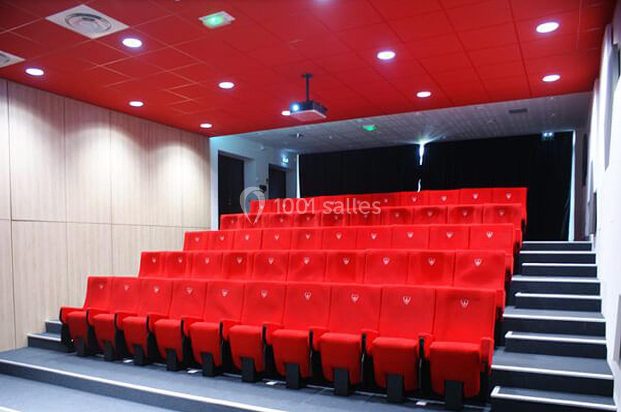 Salle de projection avec des rangées de sièges rouges, un écran noir et un plafond équipé de luminaires.