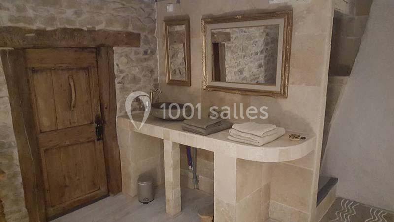 Salle de bain rustique avec murs en pierre, vasque en pierre sur un plan en pierre et miroir encadré en bois.