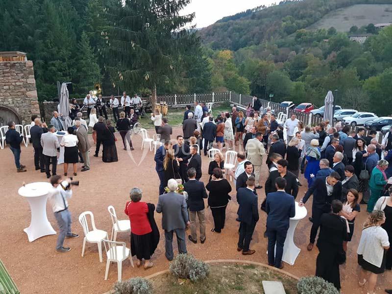 Groupe de personnes rassemblées en extérieur lors d'un événement, avec des tables hautes et un paysage boisé en arrière-plan.