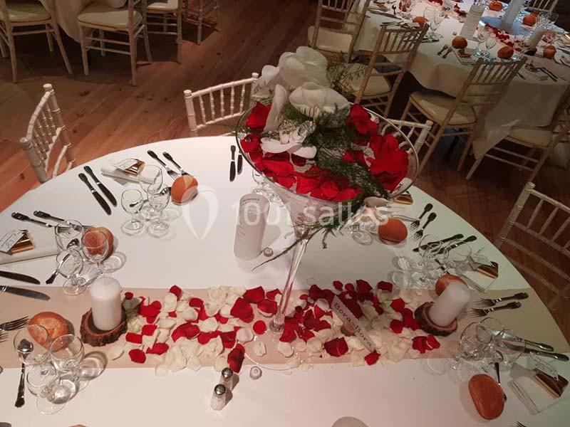 Table de réception décorée avec des pétales rouges et blancs, un centre de table floral et des couverts disposés.