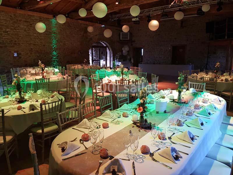Salle de réception décorée avec des tables dressées, chaises en bois, éclairage coloré et lanternes suspendues.