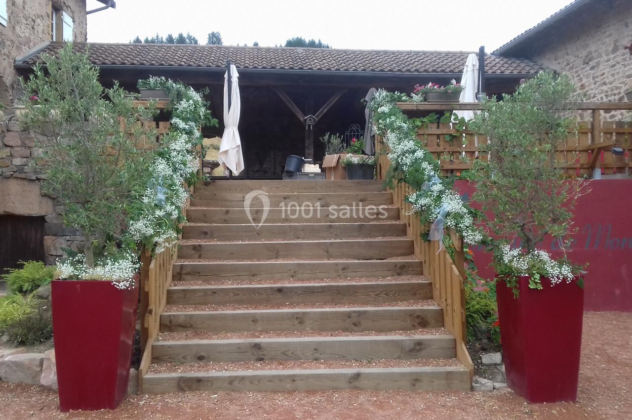 Escalier en bois bordé de jardinières rouges et de plantes fleuries, menant à une terrasse couverte en pierre.
