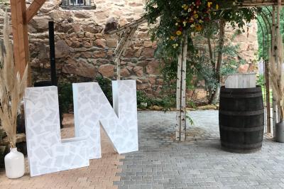 Structure en bois avec décorations de mariage, incluant des lettres blanches, un tonneau et des fleurs suspendues.