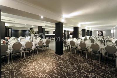 Une femme échange avec une réceptionniste dans le hall lumineux d'un hôtel, avec un coin salon visible en arrière-plan.