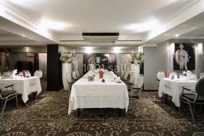 Une femme échange avec une réceptionniste dans le hall lumineux d'un hôtel, avec un coin salon visible en arrière-plan.