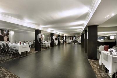 Une femme échange avec une réceptionniste dans le hall lumineux d'un hôtel, avec un coin salon visible en arrière-plan.