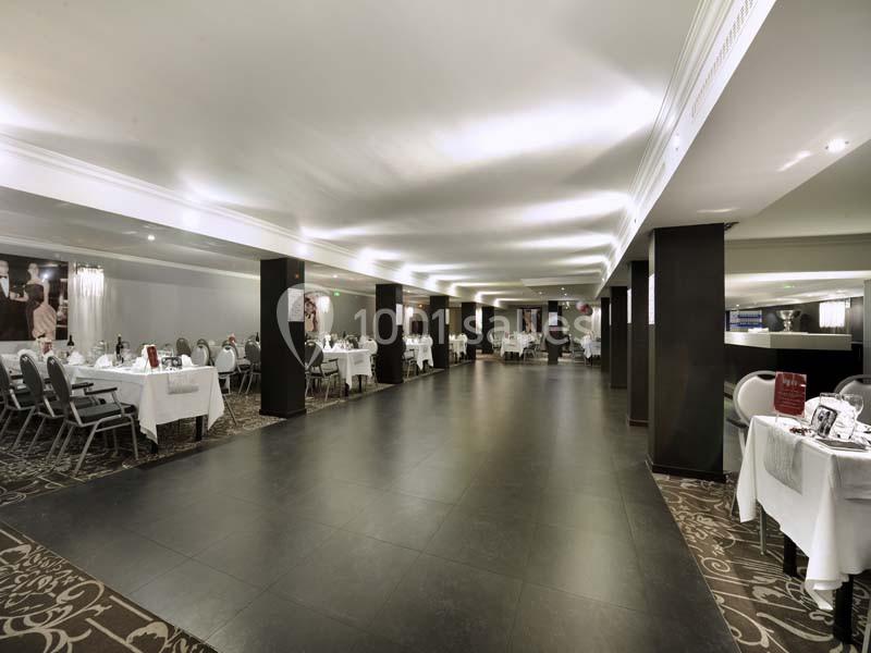 Salle de réception spacieuse avec tables dressées, chaises grises et éclairage tamisé.