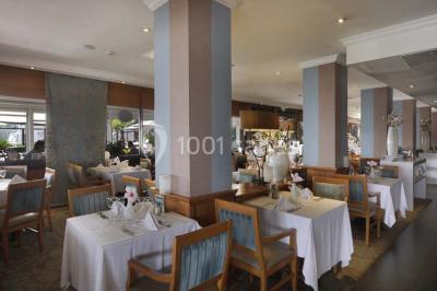 Une femme échange avec une réceptionniste dans le hall lumineux d'un hôtel, avec un coin salon visible en arrière-plan.