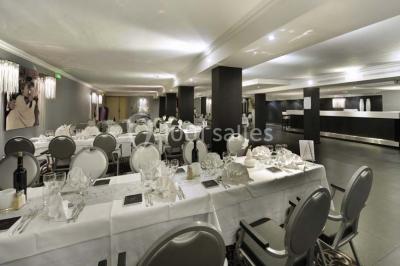 Une femme échange avec une réceptionniste dans le hall lumineux d'un hôtel, avec un coin salon visible en arrière-plan.