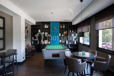 Une femme échange avec une réceptionniste dans le hall lumineux d'un hôtel, avec un coin salon visible en arrière-plan.