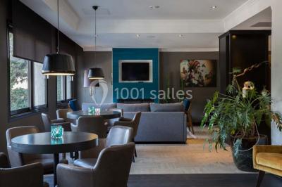 Une femme échange avec une réceptionniste dans le hall lumineux d'un hôtel, avec un coin salon visible en arrière-plan.