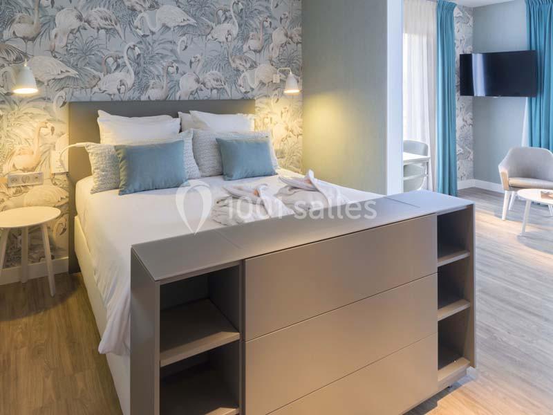 Chambre lumineuse avec lit double, décoration murale à motifs de flamants roses, mobilier moderne et télévision murale.