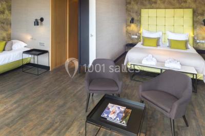 Une femme échange avec une réceptionniste dans le hall lumineux d'un hôtel, avec un coin salon visible en arrière-plan.