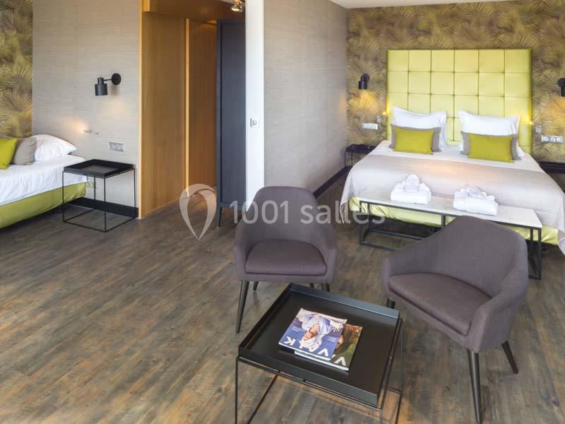 Chambre d'hôtel moderne avec deux lits, coin salon, sol en bois et décoration murale à motifs.