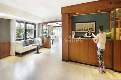 Une femme échange avec une réceptionniste dans le hall lumineux d'un hôtel, avec un coin salon visible en arrière-plan.