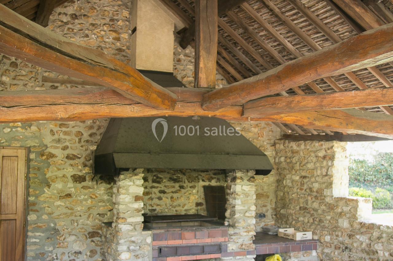 Abri en pierre avec toit en bois, abritant un barbecue en briques et des accessoires de jardinage.