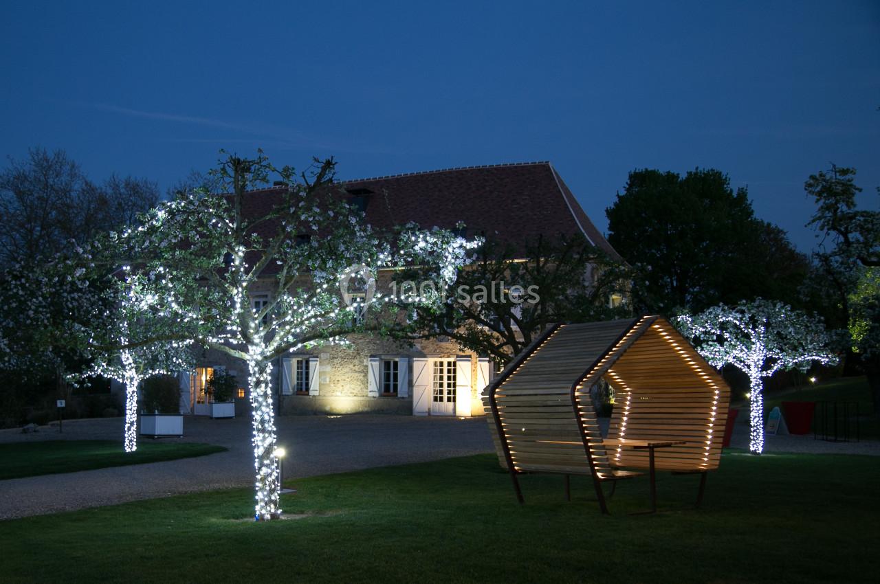 Jardin illuminé de nuit avec des arbres décorés de guirlandes lumineuses et une structure en bois moderne au premier plan.