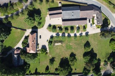 Vue aérienne d'un domaine avec bâtiments, allées, jardins et espaces verts entourés d'arbres.