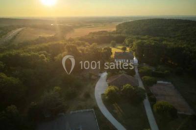 Vue aérienne d'un domaine entouré de forêts et de champs au coucher du soleil, avec des bâtiments et des allées visibles.