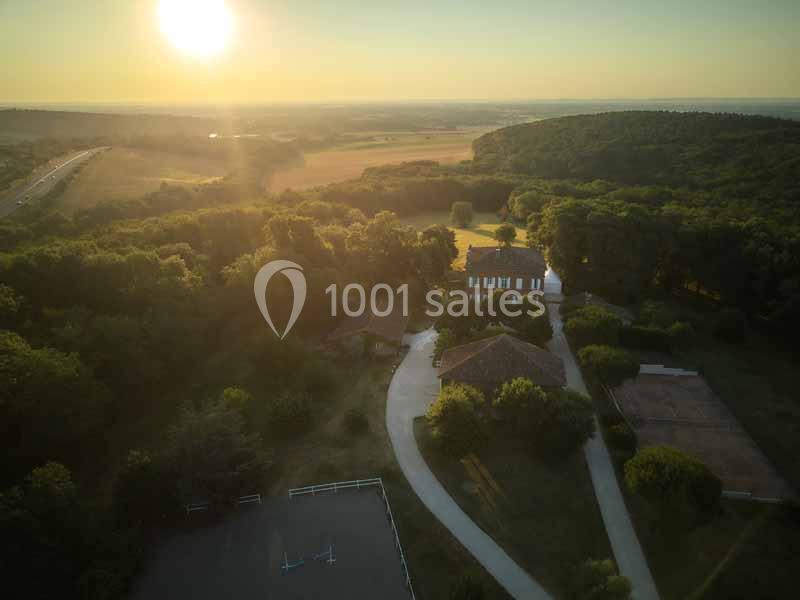 Vue aérienne d'un domaine entouré de forêts et de champs au coucher du soleil, avec des bâtiments et des allées visibles.
