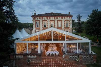 Vue aérienne d'un domaine entouré de forêts et de champs au coucher du soleil, avec des bâtiments et des allées visibles.